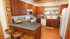 A kitchen with wooden cabinets, a central island with stools, a stove, a dishwasher, and a refrigerator. - Secluded, Cozy Cabin on 10 Acres of Woods ~16 mi to Slopes & Pet Friendly! (Whitingham)
