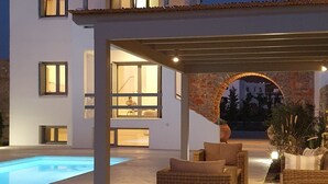 Et overdækket udendørs område med en swimmingpool, fletmøbler og en stenhvælv, der fører til en bygning.