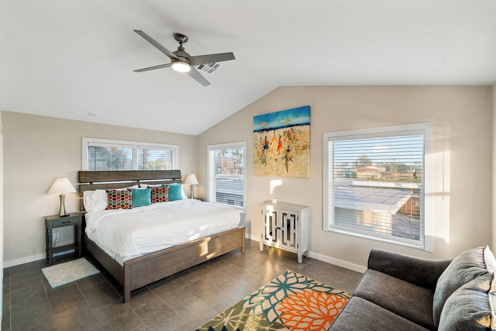 A bedroom with a bed, a ceiling fan, a nightstand, a dresser, a window, and a painting.