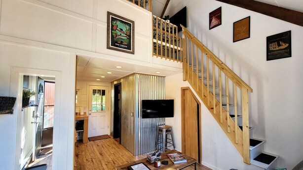 A spacious living area with a wooden staircase, a TV mounted on the wall, and framed pictures. - The Davis Loft - Perfect Location (Davis)