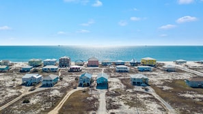 A coastal area with multiple buildings, some elevated on stilts, and a clear view of the ocean.