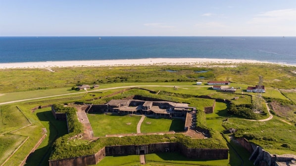 An aerial view of a historical fort with surrounding grassy areas and a beach in the background.