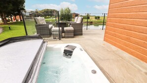 A hot tub with a metal cover, surrounded by outdoor furniture and a wooden wall. - Henry Haven (Preston)