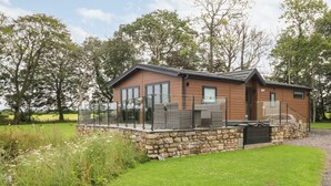 A lodge with a stone foundation, large windows, and a covered outdoor seating area. - Henry Haven (Preston)