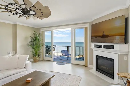 A living room with a white fireplace, a flat-screen TV, a sofa, and a ceiling fan.