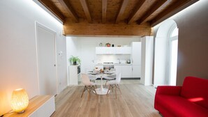 Una cocina moderna con armarios blancos, una mesa de comedor con sillas y un sofá rojo en una habitación luminosa con vigas de madera en el techo.