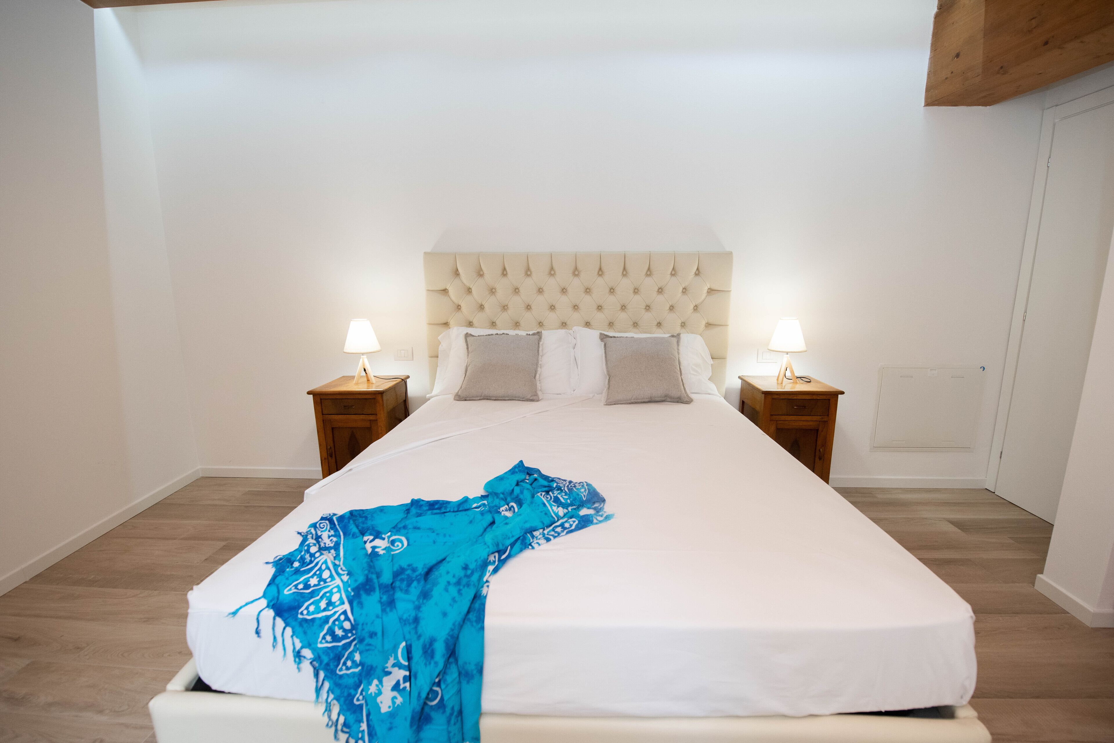 A neatly made bed with a white mattress and a blue blanket, two bedside lamps, and a wooden headboard.