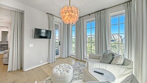 Ein modernes Wohnzimmer mit großem Fenster, Fernseher und einem gesteppten Hocker.