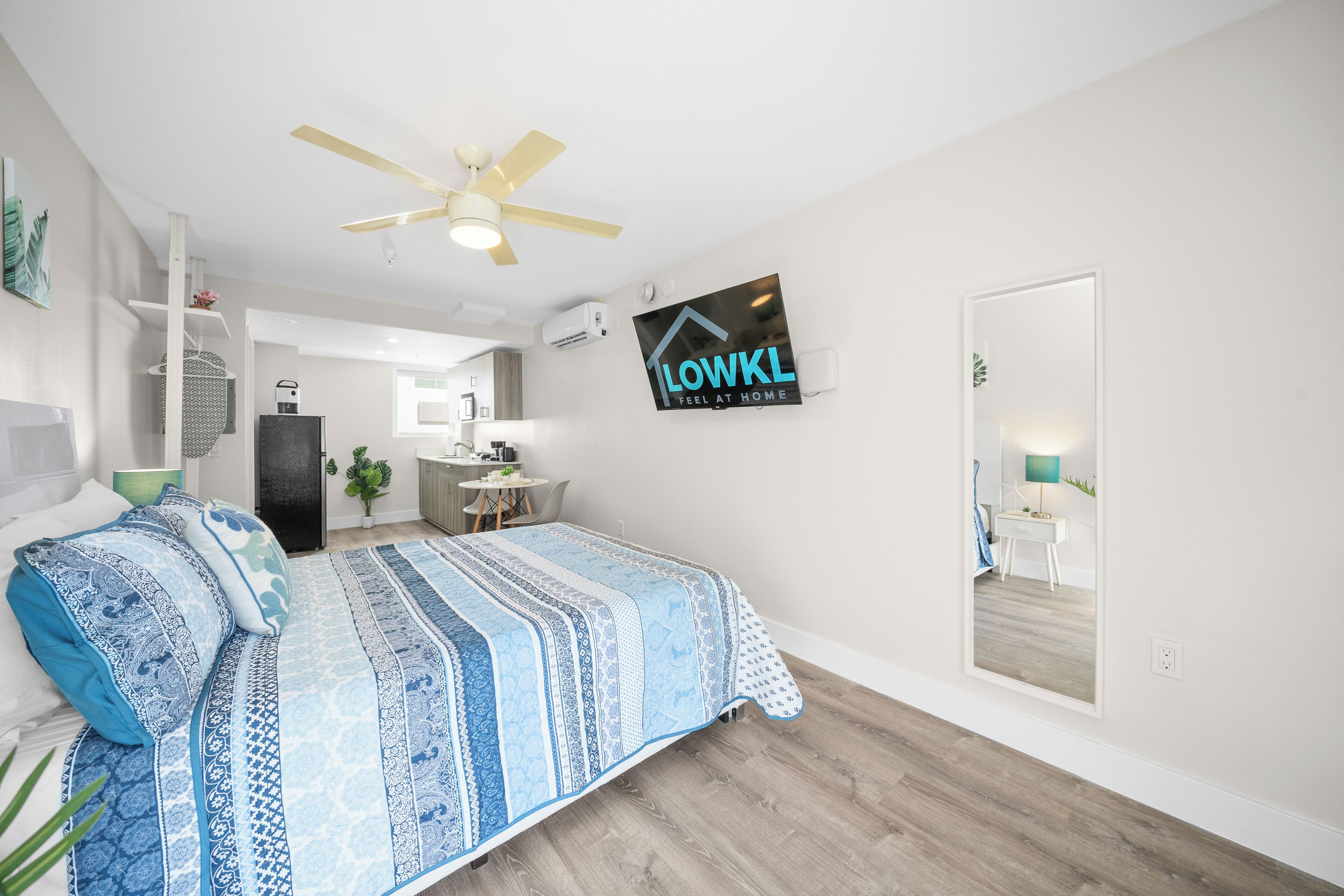 A modern bedroom with a bed, a ceiling fan, and a sign that reads "LOWKL FEEL AT HOME".