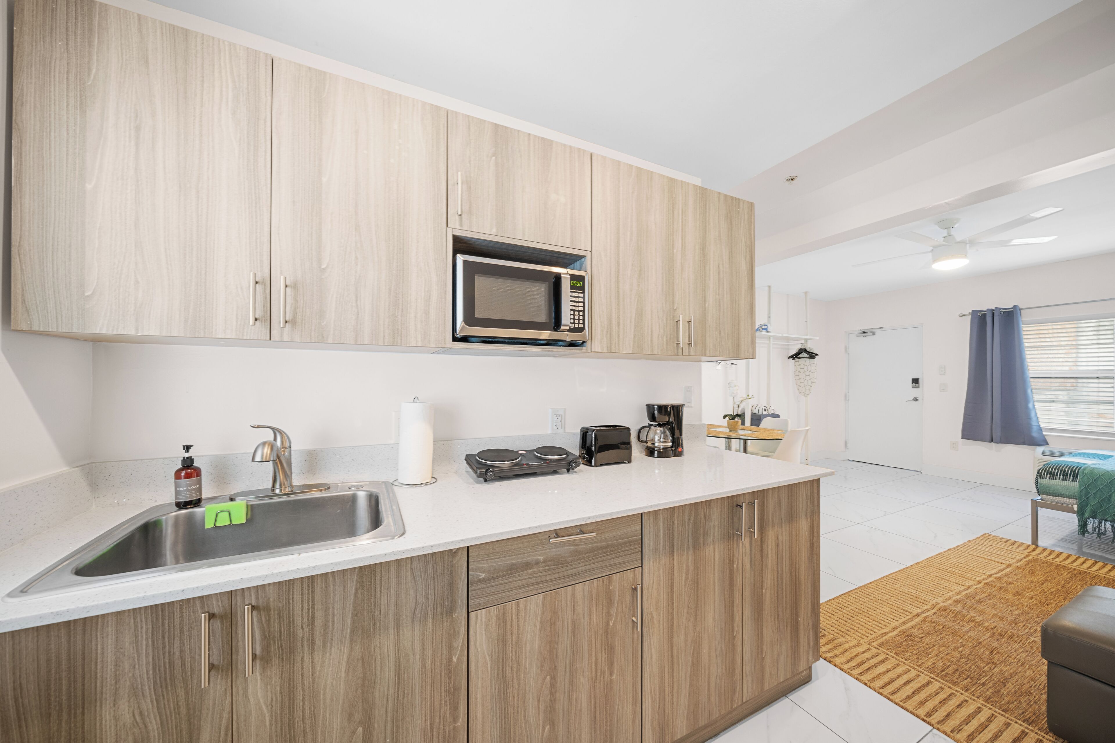 Una cocina moderna con armarios de madera, un lavamanos de acero inoxidable, microondas, tostadora y cafetera.