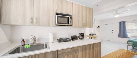 A modern kitchen with wooden cabinets, a stainless steel sink, a microwave, a toaster, and a coffee maker.