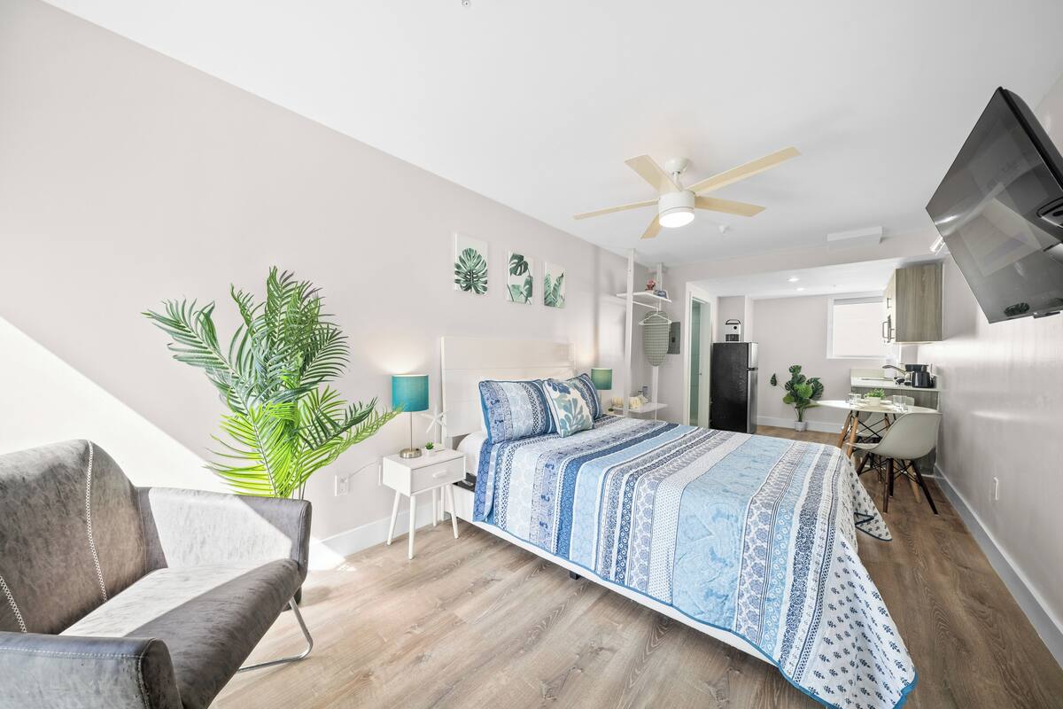A modern bedroom with a large bed, a desk, a chair, a ceiling fan, and a TV.