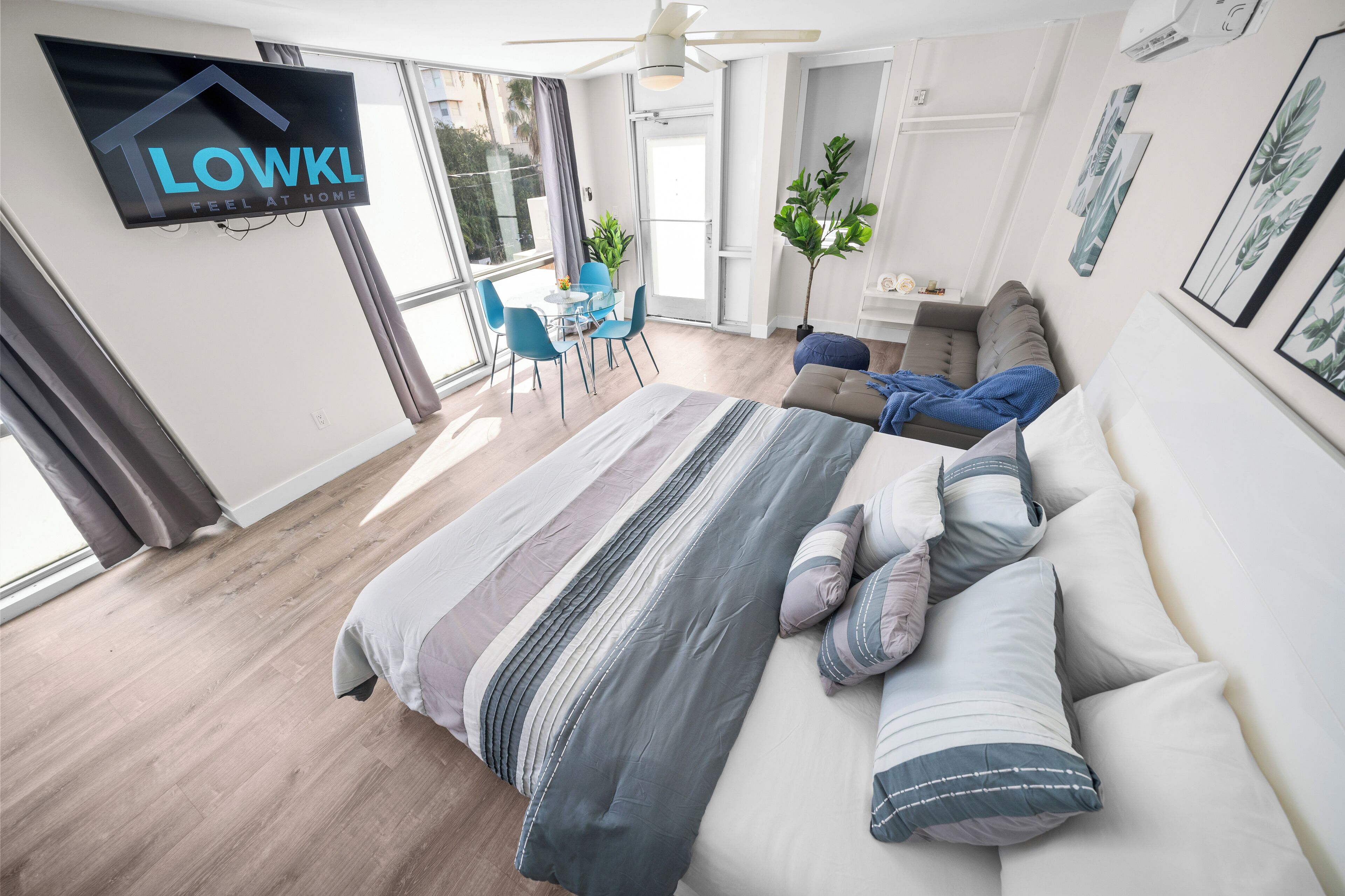 A modern bedroom with a large bed, a dining area with chairs, a small table, and a TV mounted on the wall.