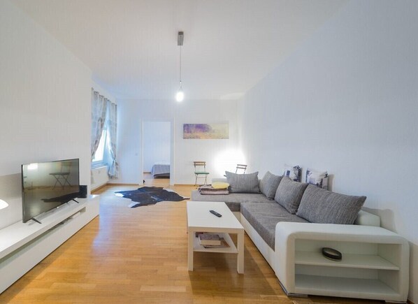 Un salon moderne avec un téléviseur à écran plat, une table basse blanche, un canapé gris et une console blanche.