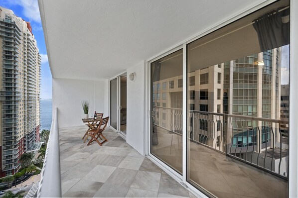 A balcony with a table and chairs, large sliding glass doors, and a view of high-rise buildings. - Luxury Unit - Perfect location with parking (Miami)
