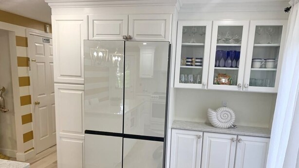 A kitchen with white cabinetry, a double-door refrigerator, and a glass-fronted cabinet with dishes. - Serene Haven w/ No Shared Spaces | Cape Cod (Marston Mills)