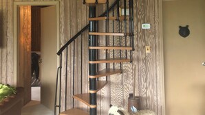 Un escalier en colimaçon avec des marches en bois et des rampes noires, une décoration représentant un ours sur le mur, et un animal en peluche sur un tapis.