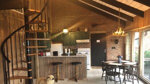 Une cuisine rustique avec un escalier en colimaçon, un coin repas avec des chaises en bois et une grande fenêtre.