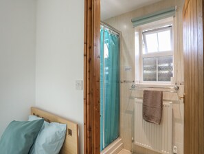 Ett badrum med dusch, ett fönster, en handduksställning och en säng med kuddar.