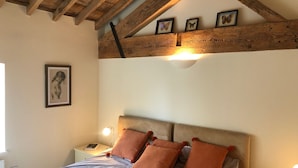 Un dormitori amb sostre de fusta, un llit amb capçalera i tres quadres al mur.