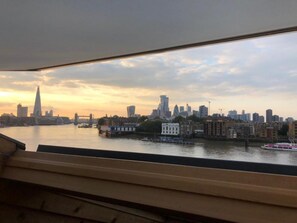 Blick auf eine Stadtlandschaft bei Sonnenuntergang, aufgenommen durch ein Fenster, mit einem Fluss, mehreren Gebäuden und einer Brücke.