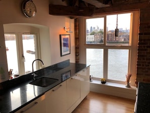 A kitchen with a black countertop, white cabinets, a sink, and a window overlooking a cityscape. - Riverside Penthouse Apartment (London)