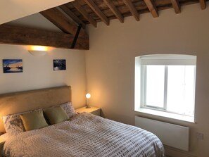 Ein Schlafzimmer mit einem Bett, einem Nachttisch, einem Fenster und Holzbalken an der Decke.