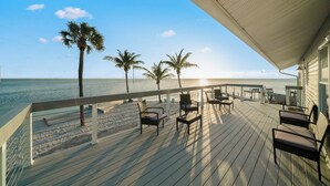 A wooden deck with outdoor seating, palm trees, and a view of the ocean. - Chasing Pelicans #9 - Waterfront - Sunset Views (Cocoa Beach)