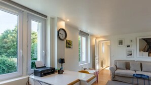 Un saló modern amb grans finestres, un sofà, una taula de centre i un escriptori amb una impressora.
