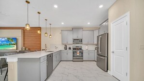 Une cuisine moderne avec des meubles gris, un îlot central, des appareils en acier inoxydable et des luminaires suspendus.