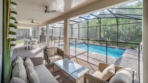 Une vaste terrasse dotée d’une piscine couverte par une verrière, de meubles en osier et offrant une vue sur la forêt environnante.