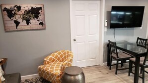 Un salon décoré d’une œuvre d’art représentant une carte du monde, avec une porte blanche, une table à manger en verre entourée de chaises, et une grande table ronde en métal.