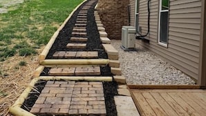 Un chemin menant à une maison avec un mur en pierre et une terrasse en bois.