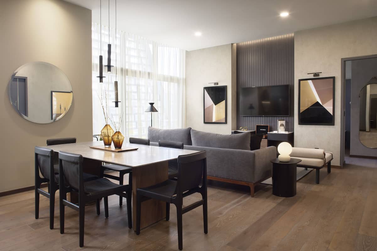 A modern living room with a dining area, grey sofa, flat-screen TV, and artwork on the walls.