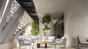 Un espacio interior moderno con techo alto, diseño geométrico en el techo y una zona de estar central con una mesa redonda.
