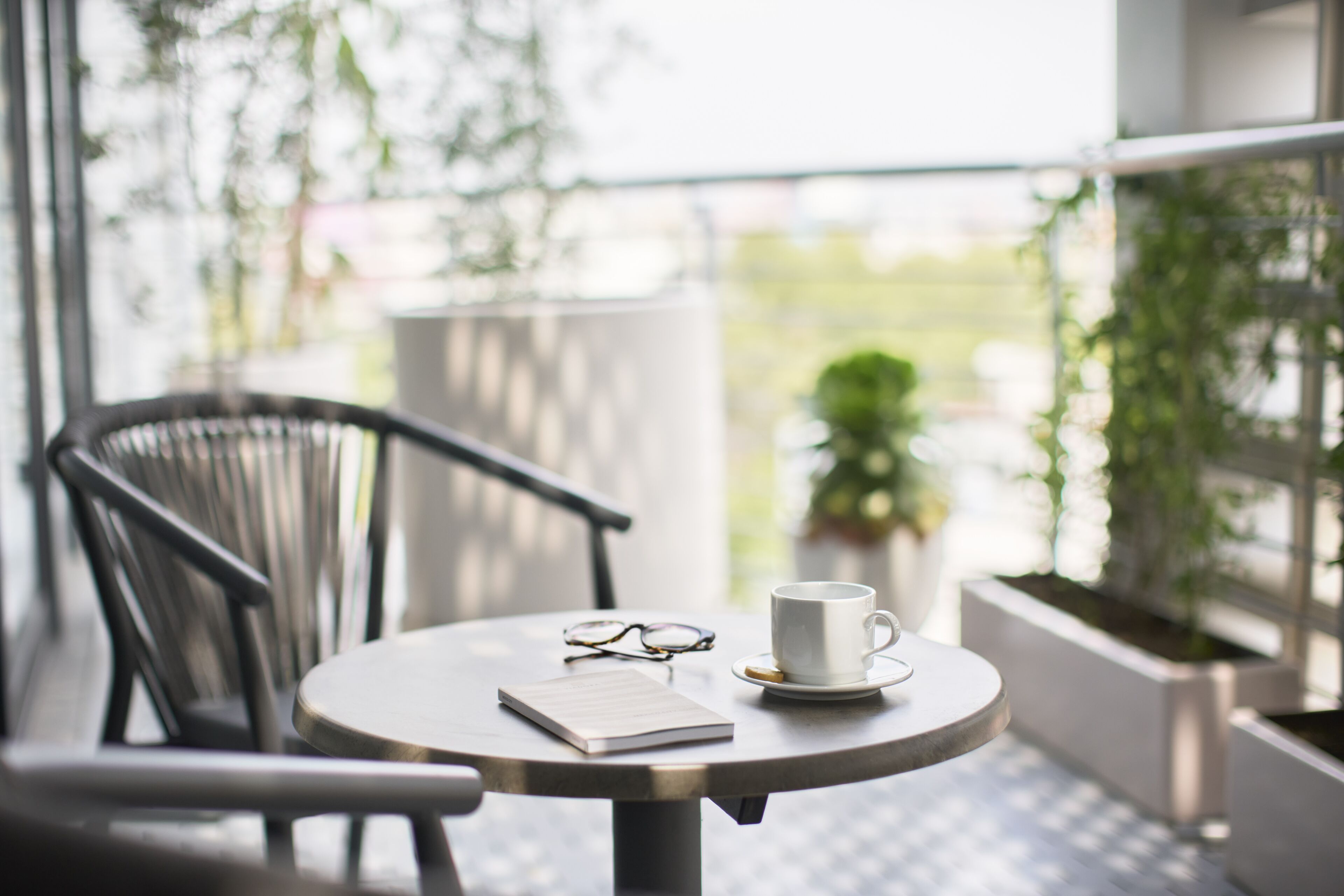 A round table with a white cup, a pair of glasses, and a notebook on it.