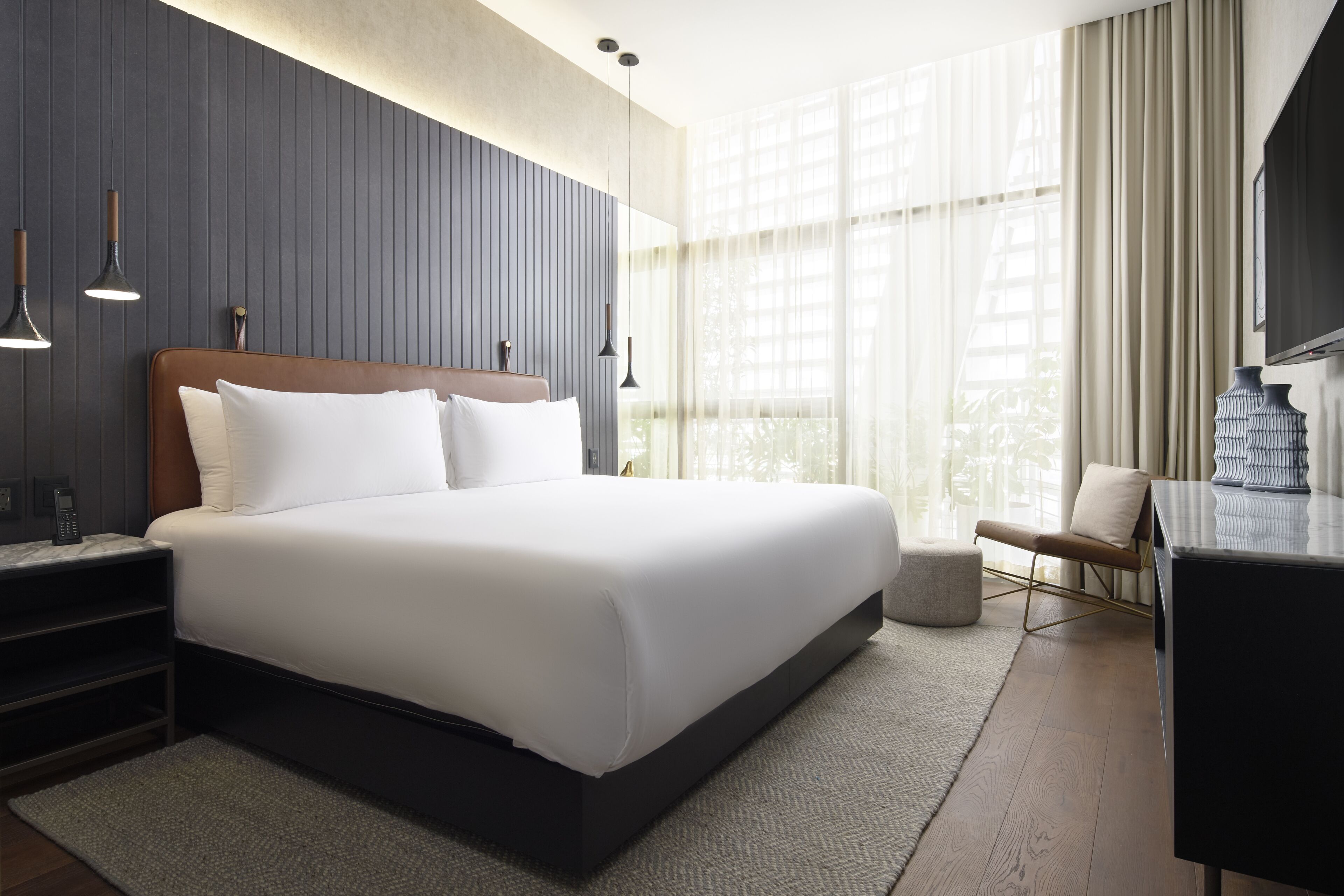 Una habitación de hotel moderna con una cama grande, lámparas de noche, un escritorio y un ventanal con cortinas.