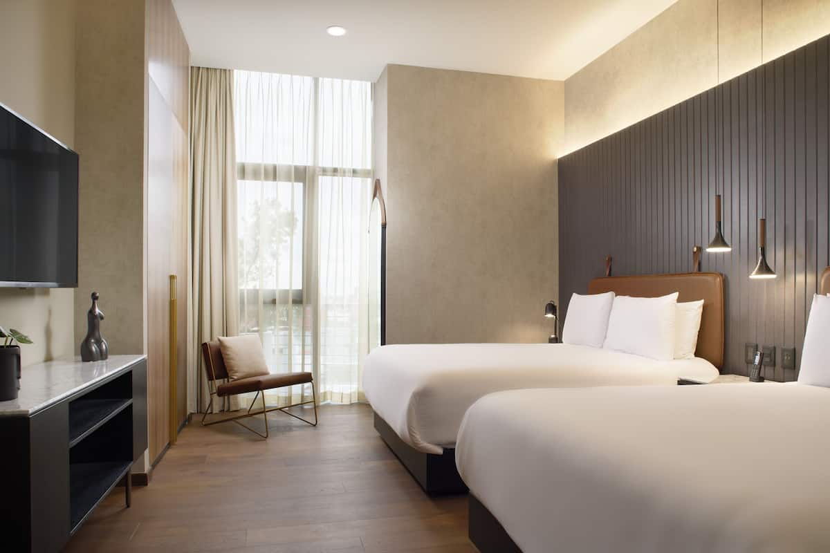 A hotel room with two beds, a TV, a desk, and a chair.