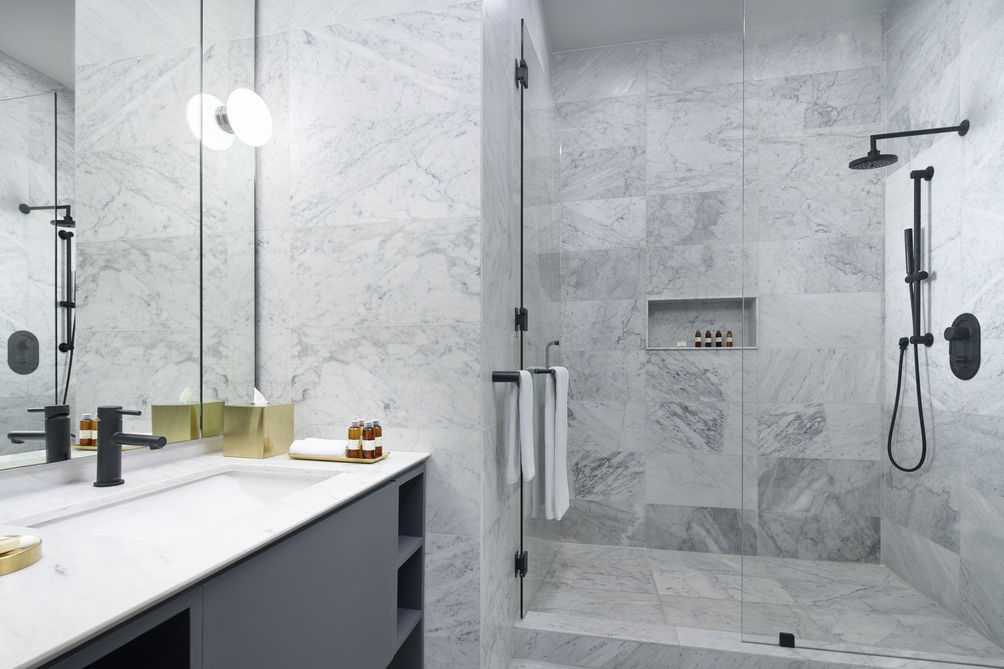 A modern bathroom with a marble shower, a large mirror, and a white sink.