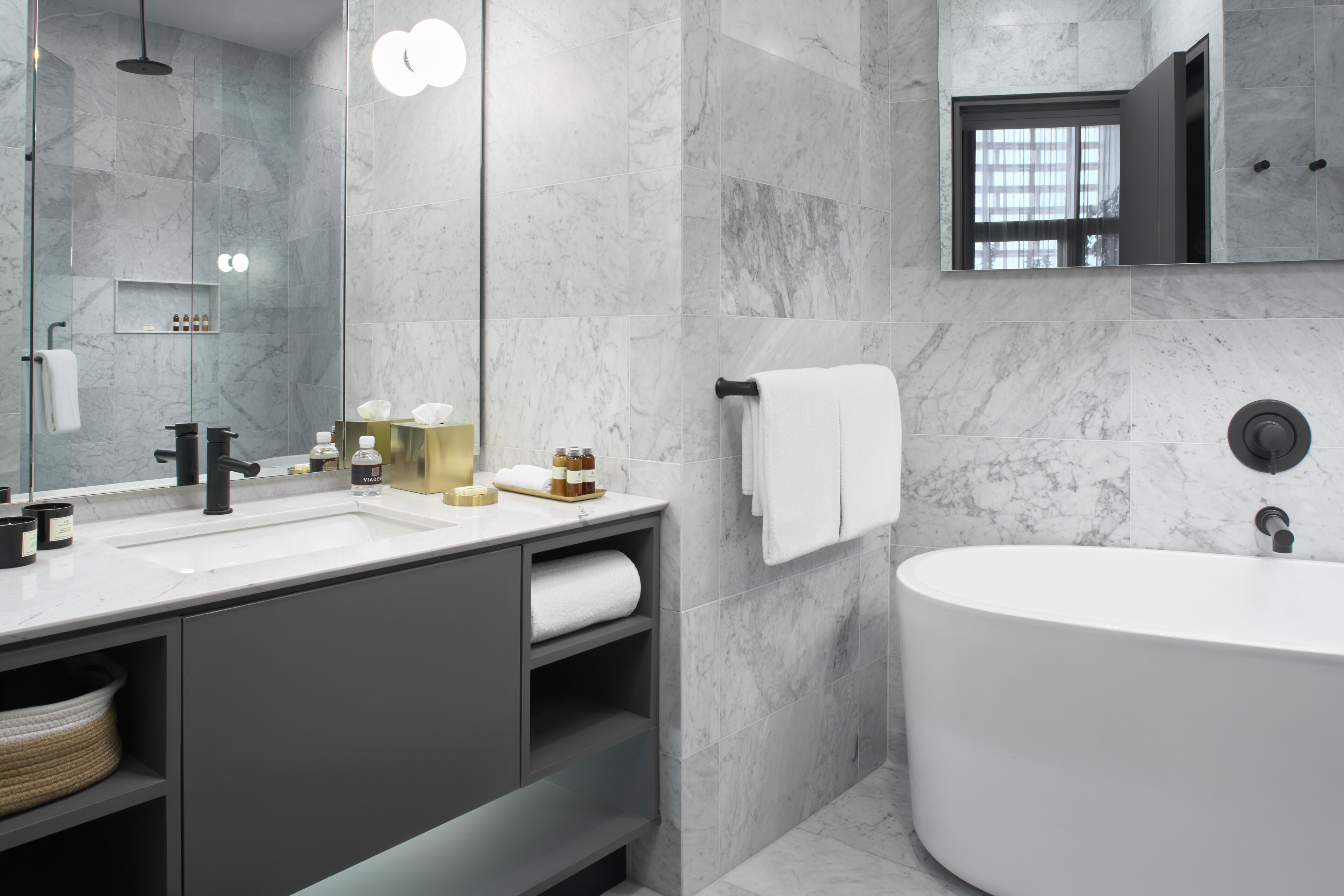 A modern bathroom with a large bathtub, a vanity with a mirror, and marble walls.
