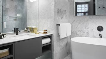 A modern bathroom with a large bathtub, a vanity with a mirror, and marble walls.