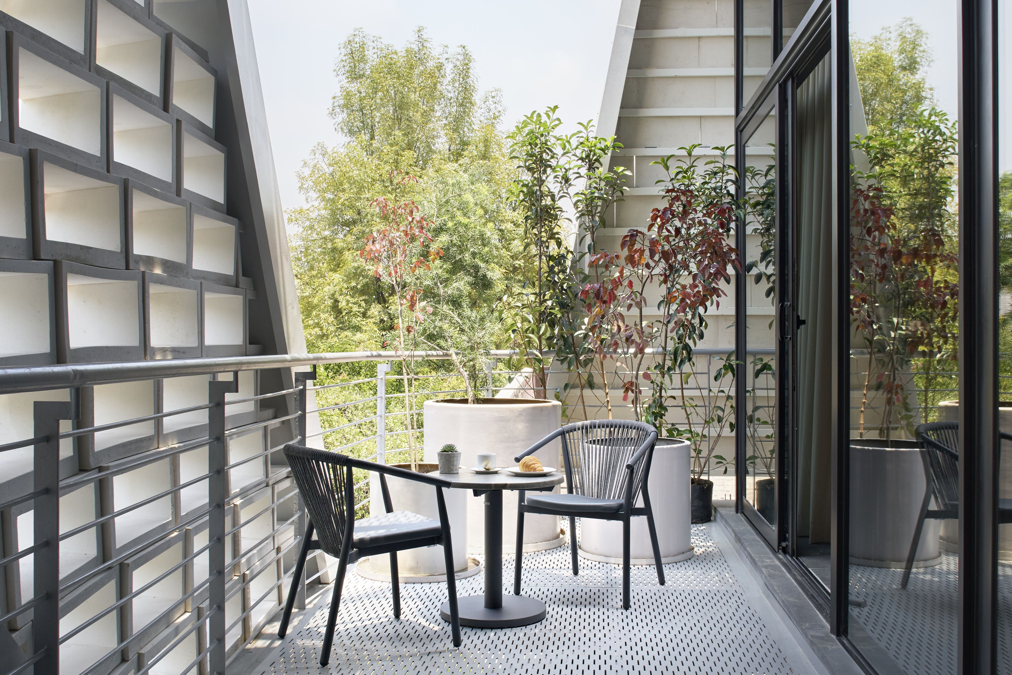 A balcony with a metal railing, a round table with two chairs, and potted plants.