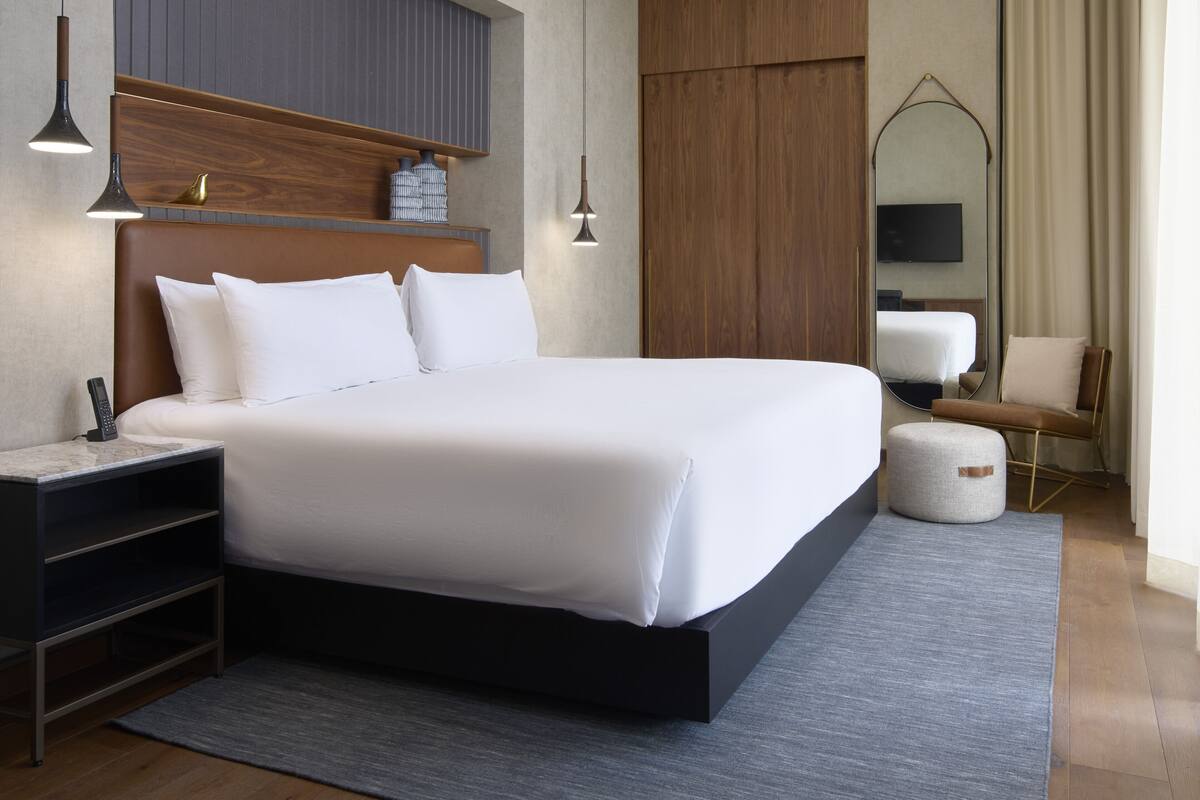 A modern hotel room with a large bed, bedside tables, a mirror, and a seating area.
