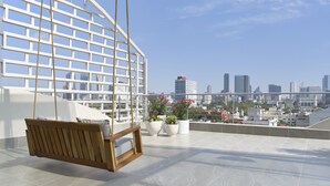 Una terraza en la azotea con una hamaca de madera, plantas en macetas y vistas al horizonte de la ciudad.