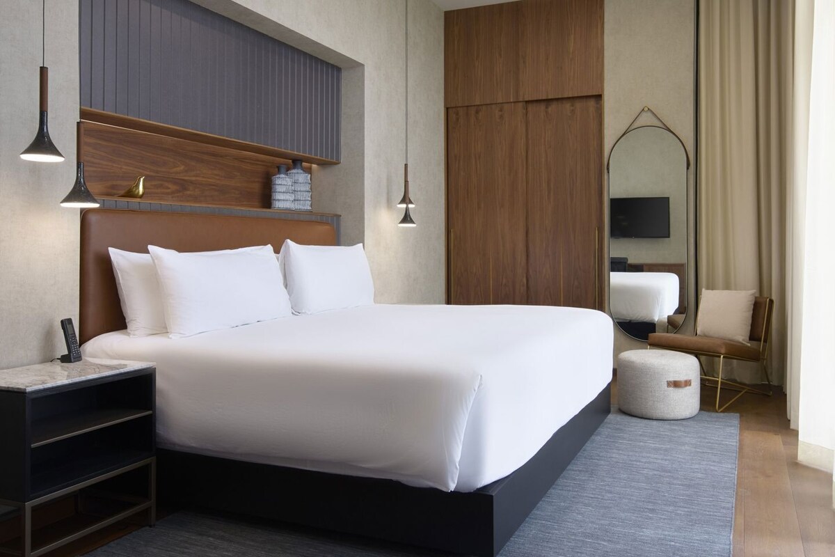 Ein modernes Hotelzimmer mit einem großen Bett, Nachttischen, einem Spiegel, einem Fernseher und einer Sitzecke.