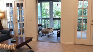 A spacious living room with a ceiling fan, a dining area with a table and chairs, and a view of a balcony with outdoor furniture. - Country Club Beach Vacation (Vero Beach)