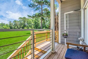 A wooden deck with a metal railing overlooking a green lawn and trees. - The Lantana Tiny Home  ~ Cottage in the Woods ~ NEW HOT TUB & DOGGY PLAY YARD (Willis)