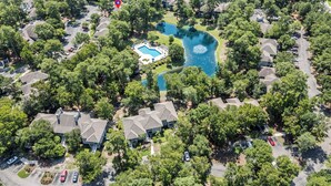 An aerial view of a residential area with houses, a swimming pool, and a pond.