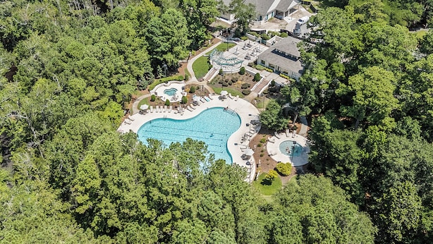 An aerial view of a residential property with a large swimming pool, multiple decks, and lush surrounding trees.