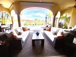 A sunlit outdoor seating area with two sofas and a coffee table, overlooking a swimming pool and lush greenery.